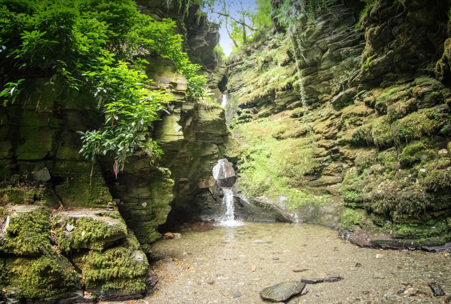 Water flows through the kieve at st nectans glen waterfall, with moss covered rocks in the deep valley either side