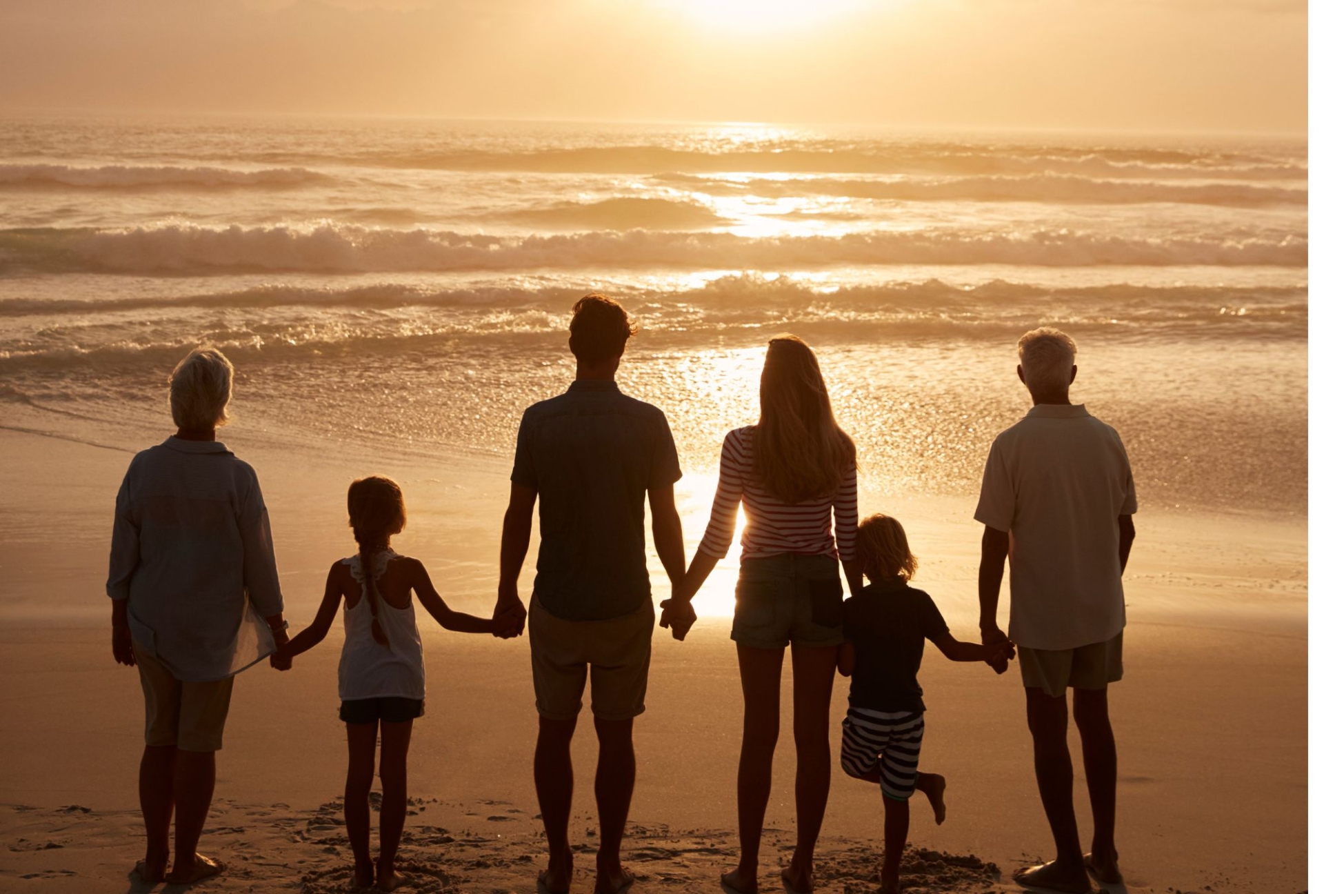 Family at sunset on the beach holding hands, 3 generations